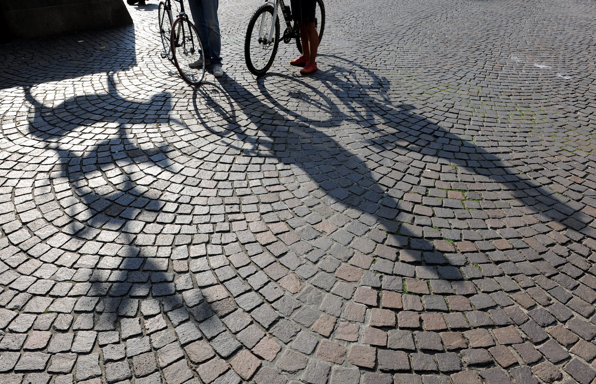 Pflastersteine, am Rand erkennt man die Beine von zwei Menschen, die ein Fahrrad schieben